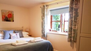A neatly made bed with pillows and folded towels, a painting on the wall, and a window with curtains.