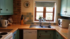 A kitchen with a brick wall, a window with a curtain, a sink, a stove, and a dishwasher.