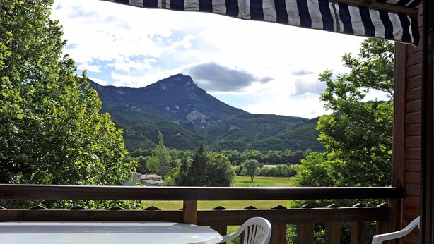 Une terrasse en bois avec une table et des chaises, offrant une vue sur un paysage montagneux.