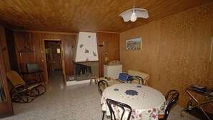 Une pièce chaleureuse avec un plafond en bois, une table à manger ronde recouverte d’une nappe à motifs floraux et un téléviseur placé dans un coin.