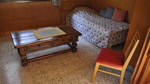 Une petite pièce agréable et chaleureuse, avec un lit en bois, une table en bois sur laquelle est posée une nappe, une chaise rouge et une fenêtre avec des rideaux.