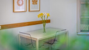 Une pièce avec un bureau blanc, deux chaises, un vase avec des fleurs jaunes et deux tableaux encadrés accrochés au mur.