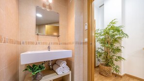 Une salle de bain avec un lavabo blanc, un miroir et une plante en bambou dans un panier tressé.