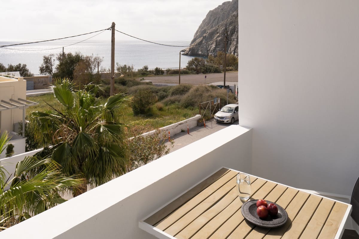 A balcony with a wooden table, a glass, and a plate of fruit.