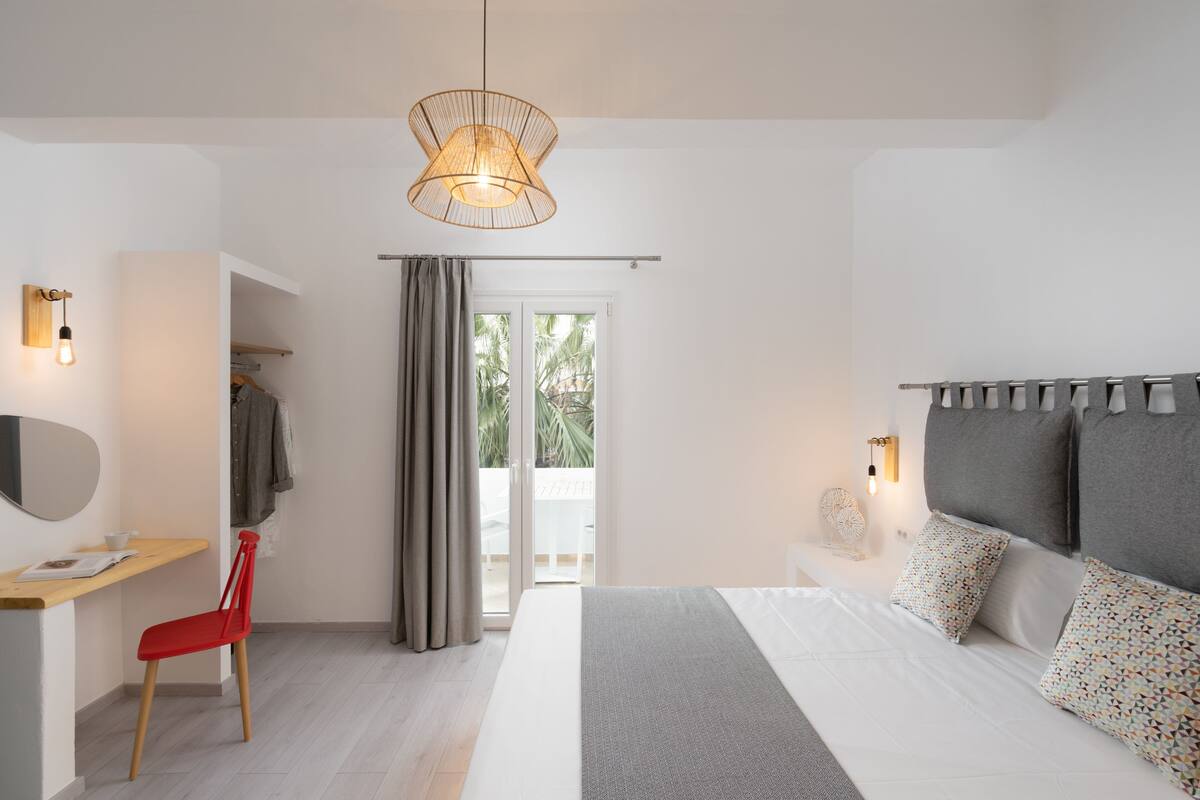 A modern bedroom with a bed, bedside table, chair, and a view of the outdoors through a sliding door.