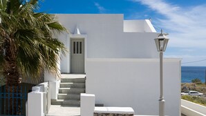 A white building with a stone wall and a palm tree. - Sunray Lodgings (Santorini)