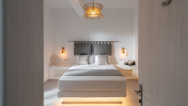 A modern bedroom with a large bed, a unique pendant light, and a minimalist design. - Sunray Lodgings (Santorini)