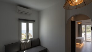 A modern room with a built-in bench, a large window with a view, an air conditioning unit, and a hanging light fixture. - Sunray Lodgings (Santorini)