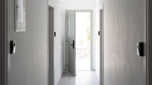 A hallway with white walls, a ceiling light, and a door leading to an outdoor area. - Sunray Lodgings (Santorini)