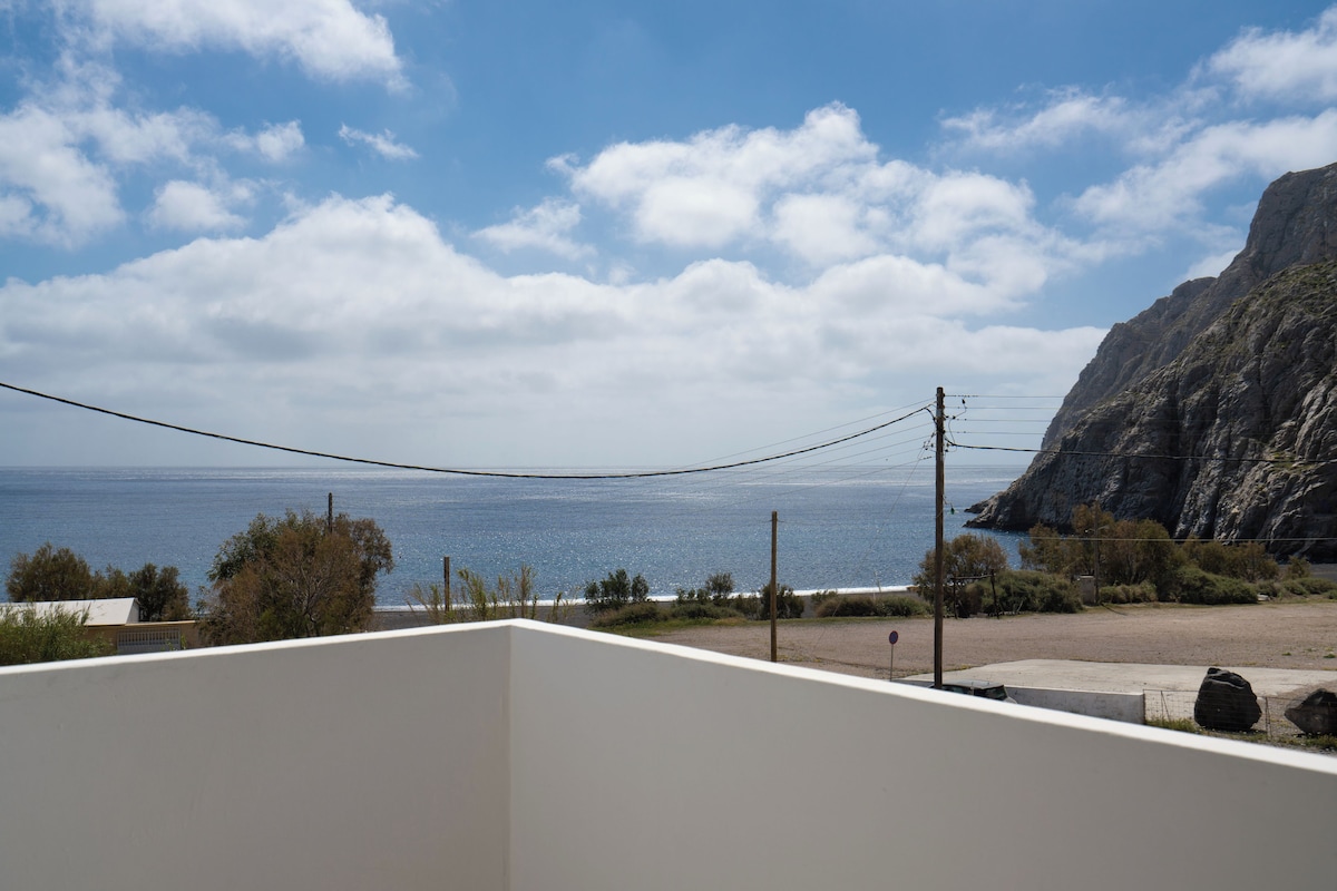A coastal view with a clear sky, a beach, and a rocky cliff.