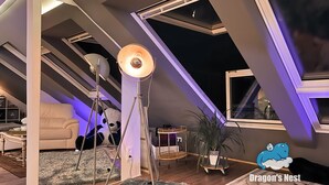 A loft-style room with a sloped ceiling, large windows, and a cozy seating area. - Dragons Nest: Cozy & Modern Attic Loft Nuremberg (Schwaig bei Nuernberg)