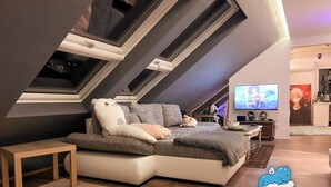 A modern loft bedroom with a sloped ceiling, a large bed, a TV, and a small desk. - Dragons Nest: Cozy & Modern Attic Loft Nuremberg (Schwaig bei Nuernberg)