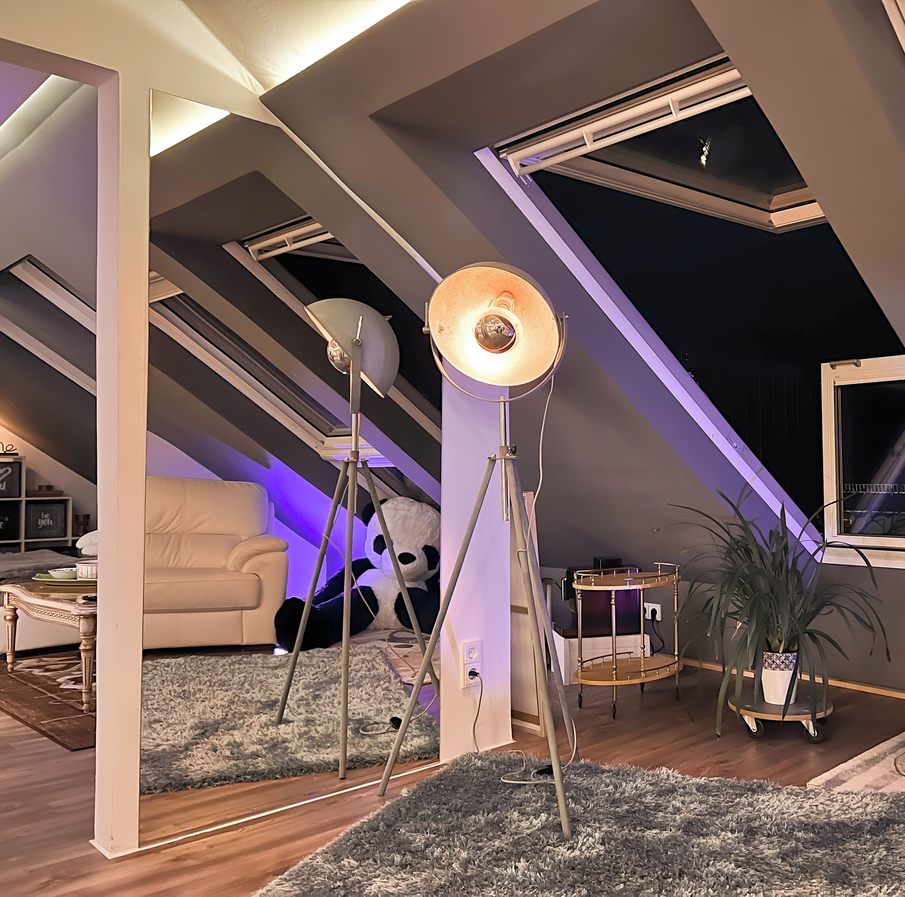 Ein Loft-Zimmer mit schrägem Dach, großen Fenstern und einer gemütlichen Sitzecke.