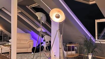 Ein Loft-Zimmer mit schrägem Dach, großen Fenstern und einer gemütlichen Sitzecke.