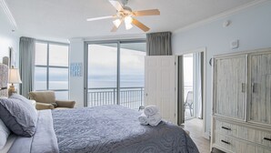 Un dormitorio con una cama grande, un ventilador de techo y vista al océano a través de la ventana.