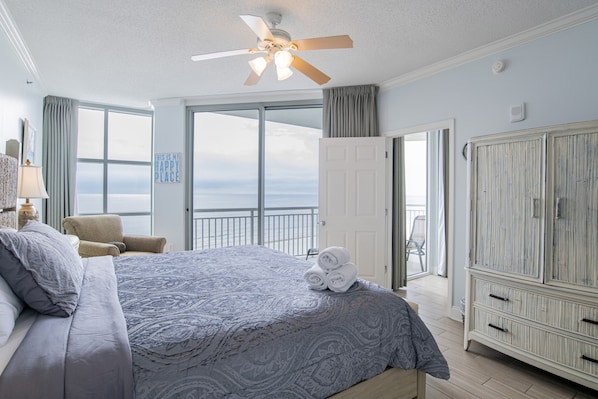 A bedroom with a large bed, a ceiling fan, and a view of the ocean through the window.