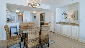 Una cocina con zona de comedor, que incluye sillas de mimbre, una mesa de vidrio y una araña.