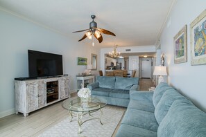 A living room with a television, a glass coffee table, a blue sofa, and a ceiling fan.