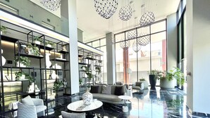 Un vestíbulo moderno con piso de mármol negro, una zona de estar con sofás y una mesa de centro, y una amplia estantería llena de plantas y objetos decorativos.