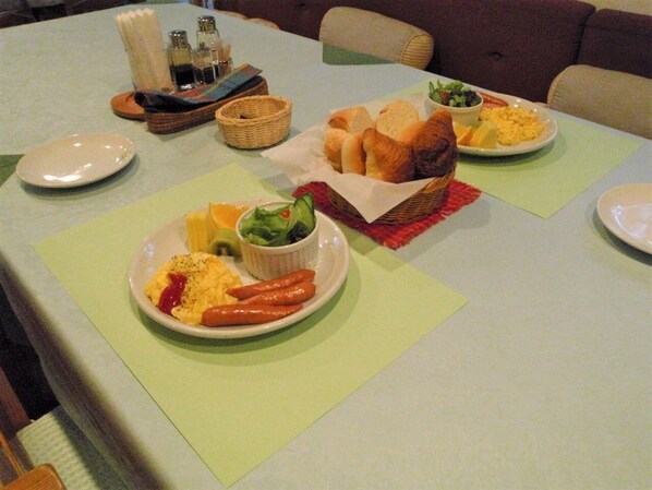 Ein Esstisch mit angerichteten Speisen, darunter Rührei, Würstchen und Gemüse. Es gibt außerdem Körbe und eine Salatschüssel.