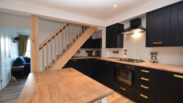Una cocina moderna con armarios oscuros, una escalera de madera y una mesa de comedor de madera.