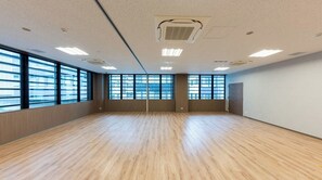 Una habitación amplia con grandes ventanales, suelo de madera y rejillas en el techo.
