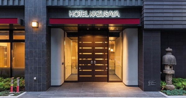 The entrance to HOTEL KAZUSA with a modern design, featuring a prominent sign and a glass door.