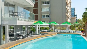 A swimming pool with a wooden deck, outdoor seating, and Heineken umbrellas.