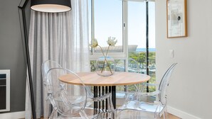 A modern dining area with a round table, clear chairs, and a view of the city through large windows.