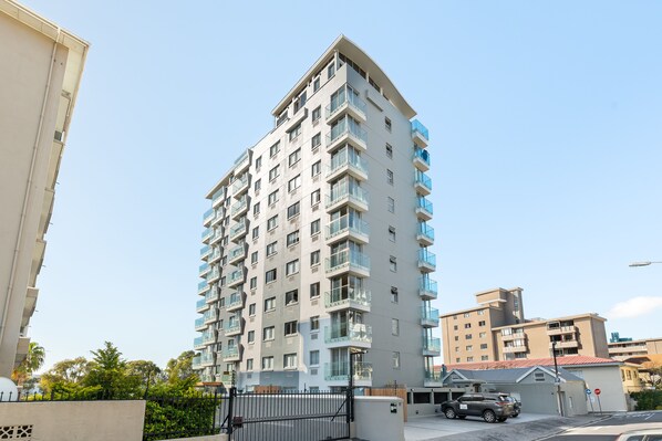 Un immeuble résidentiel de grande hauteur doté de nombreux balcons, d’une entrée sécurisée et d’un espace de stationnement.