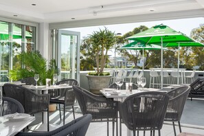 Un espace extérieur aménagé avec des tables et des chaises, un parasol vert à l’effigie de Heineken et des plantes en pot.