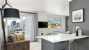 A modern kitchen with a large island, a dining area with a white table, and a sofa with patterned cushions. - Point Break | Serviced Studio | Mountain Views (Cape Town)
