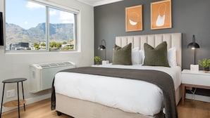 A bedroom with a large bed, a window with a city view, and two framed artworks on the wall. - Point Break | Serviced Studio | Mountain Views (Cape Town)