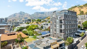 A modern urban landscape with a prominent multi-story building featuring balconies, surrounded by residential buildings and lush greenery. - Point Break | Sleek Studio | Mountain Views (Cape Town)