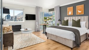 A modern bedroom with a large bed, a TV, a city view, and a dining area. - Point Break | Sleek Studio | Mountain Views (Cape Town)
