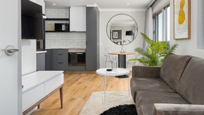 A modern living room with a grey sofa, a white coffee table, and a round mirror. - Point Break | Serviced Apartment | Pool Access (Cape Town)