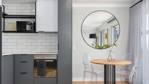 A modern kitchen with grey cabinets, a black oven, and a round mirror above a wooden table with two clear chairs. - Point Break | Serviced Apartment | Pool Access (Cape Town)
