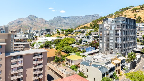 A high-rise building with multiple balconies, surrounded by other residential buildings and greenery, with a mountain in the background. - Point Break | Serviced Apartment | Pool Access (Cape Town)