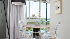 A modern dining area with a round table, clear chairs, and a vase with flowers. - Point Break | Luxe 1 Bedroom | Balcony | Netflix (Cape Town)