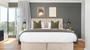 A modern bedroom with a large bed, two bedside tables, and a view of the city. - Point Break | Luxe 1 Bedroom | Balcony | Netflix (Cape Town)