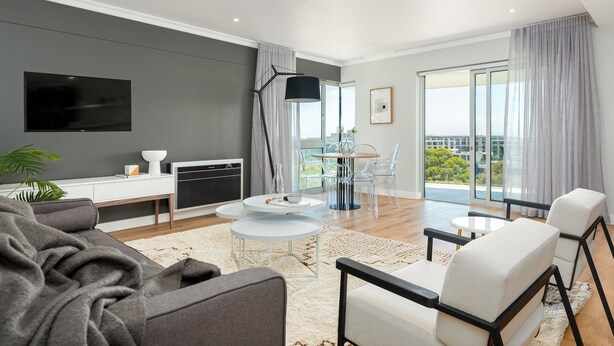 A modern living room with a flat-screen TV, a dining area with a glass table and chairs, and a balcony with a view. - Point Break | Luxe 1 Bedroom | Balcony | Netflix (Cape Town)