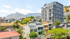 A multi-story building with balconies, surrounded by other residential buildings and greenery, with mountains in the background.