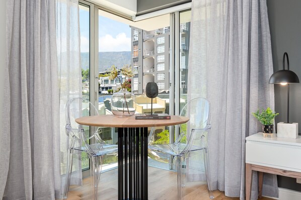 A modern room with a round table, clear chairs, a lamp, and a view of a cityscape through large windows.