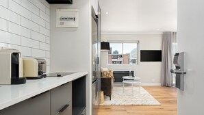 A modern kitchen with a built-in coffee machine, a flat-screen TV mounted on the wall, and a large window offering a view of the cityscape.