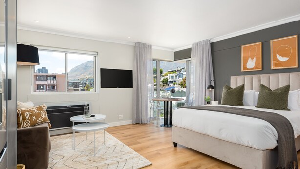 A modern hotel room with a large bed, a sofa, a small table, and a TV.