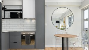 Una cocina moderna con armarios grises, un microondas negro y una mesa de comedor de madera con sillas transparentes.