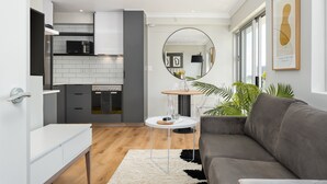 Una cocina moderna con armarios blancos, un microondas negro y un espejo redondo sobre una mesa de comedor con superficie de vidrio.