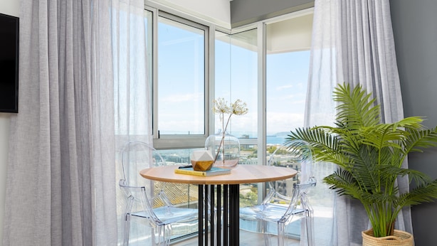 A modern room with a round table, clear chairs, a potted plant, and a view of the city through large windows. - Point Break | Ocean Views | Walk to VandA | Pool (Cape Town)