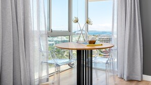 Ein modernes Zimmer mit einem runden Tisch, klaren Stühlen und Blick auf eine Stadtlandschaft durch große Fenster.