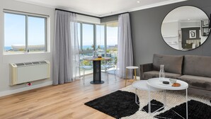 Ein modernes Wohnzimmer mit großem Fenster, einem runden Spiegel, einem grauen Sofa und einem Couchtisch.
